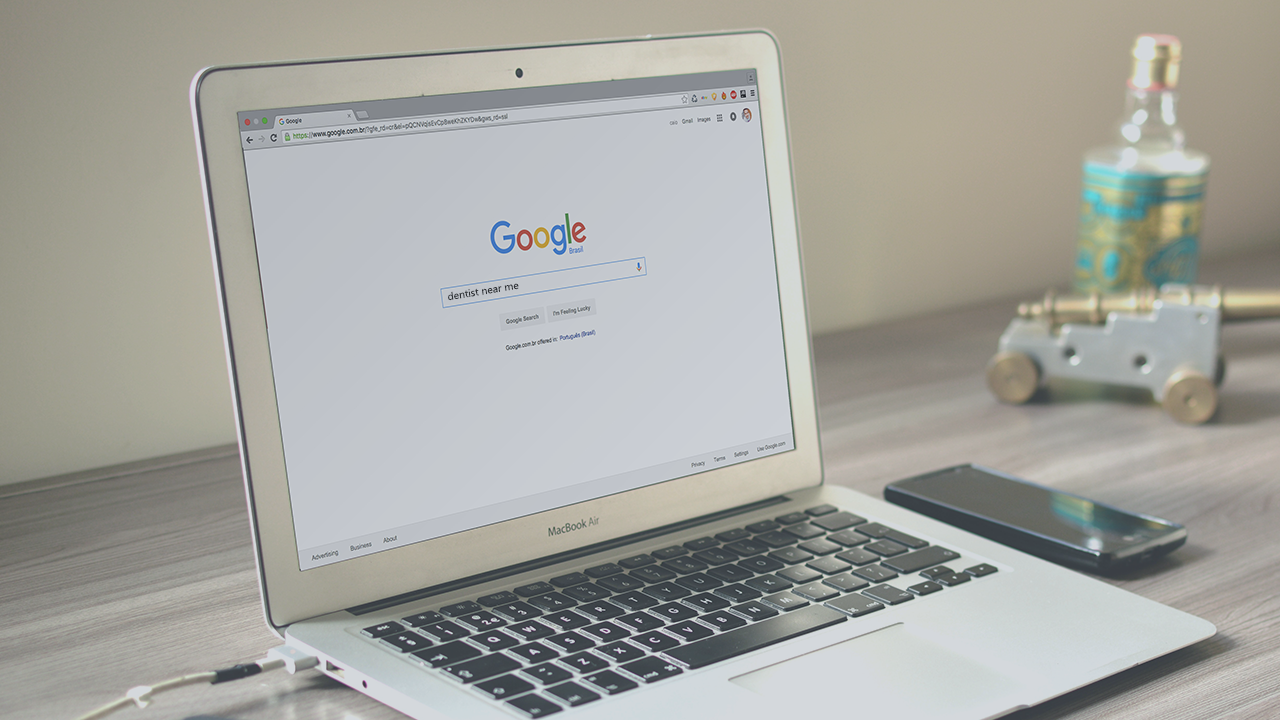 A laptop with Google open. The words "dentist near me" are typed into the Google search bar.