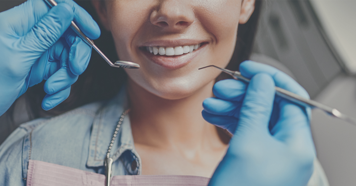 Dental patient smiling. The smile is framed by dental instruments being held by a dentist