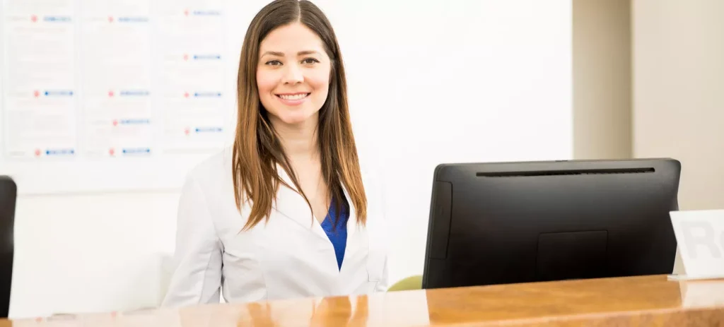 Receptionist working behind a desk and smiling at the camera.