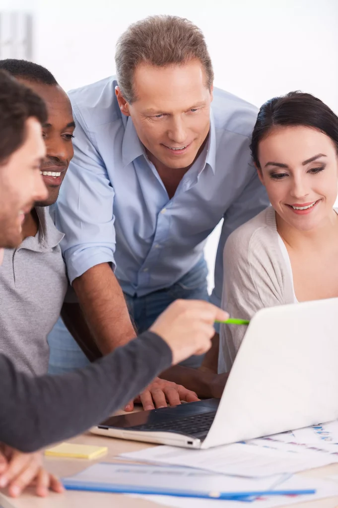 Four people looking at a laptop screen together and smiling.