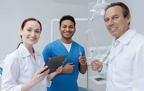 Three dental professionals in an operatory room smiling at the camera