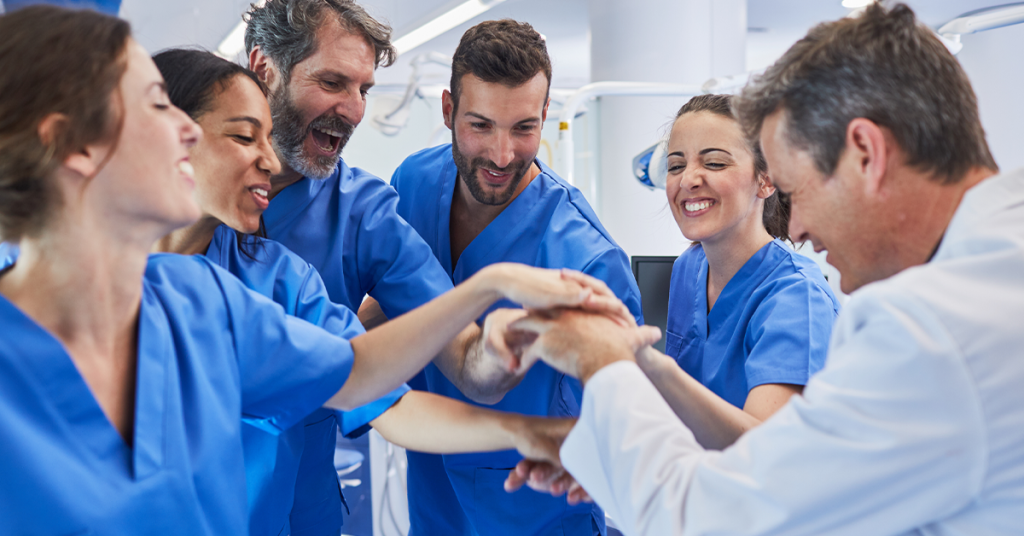 A group of dental professionals putting their hands together for a group huddle.