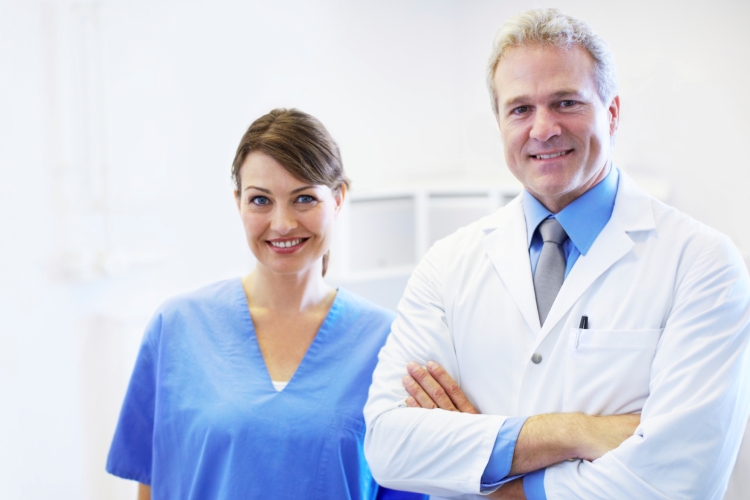 A dental assistant standing beside a dentist, both are smiling at the camera.