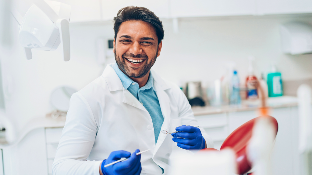 Dentist holding instruments and smiling at the camera.
